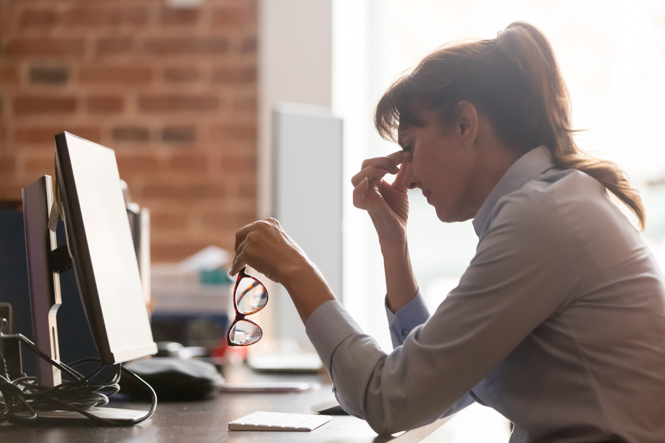 stressed middle aged woman taking off glasses at work rubbing eyes